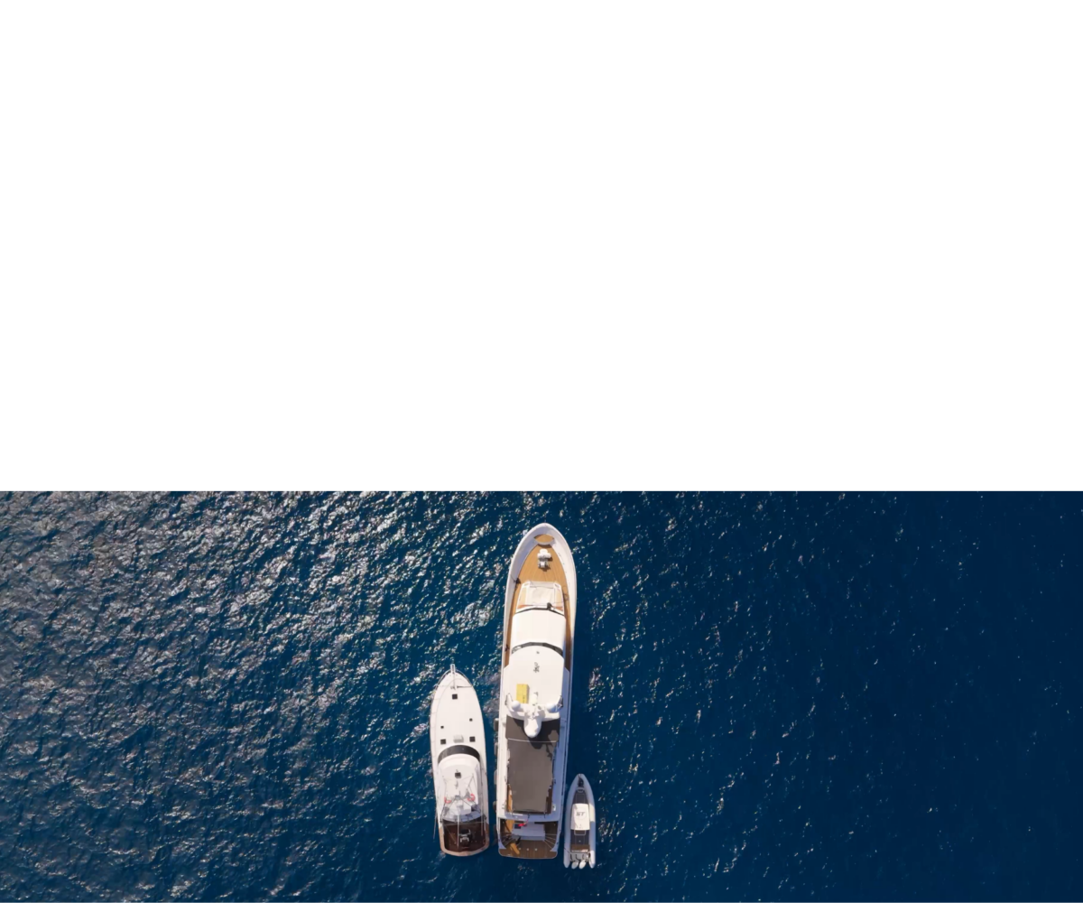 Aerial view of three boats—one large yacht and two smaller boats—anchored close together on deep blue, rippling water.