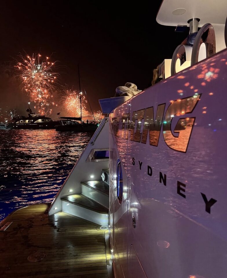 Fireworks light up the night sky over the water, viewed from the deck of a Sydney game fishing yacht.