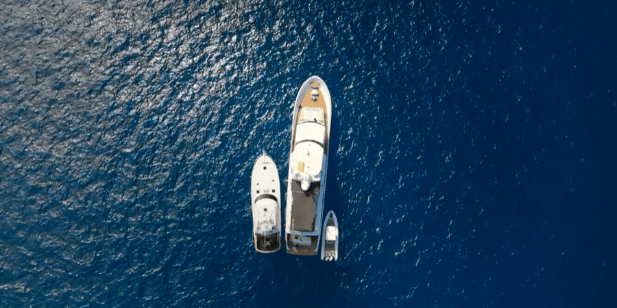 An aerial view of a large yacht with two smaller boats moored alongside it on deep blue water.