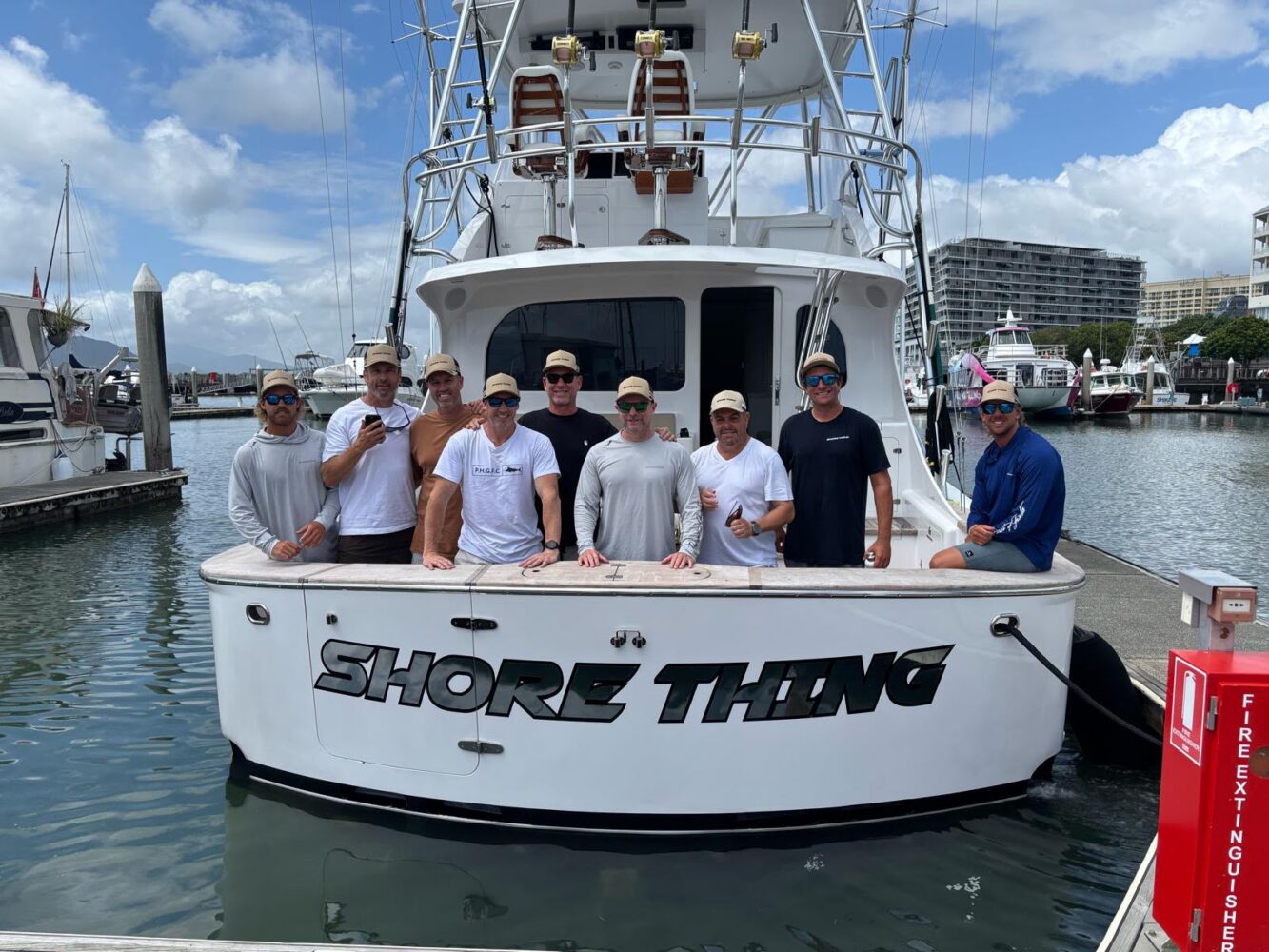 Eight men posing on the stern of a white boat named “SHORE THING” during a corporate Christmas party in Sydney.