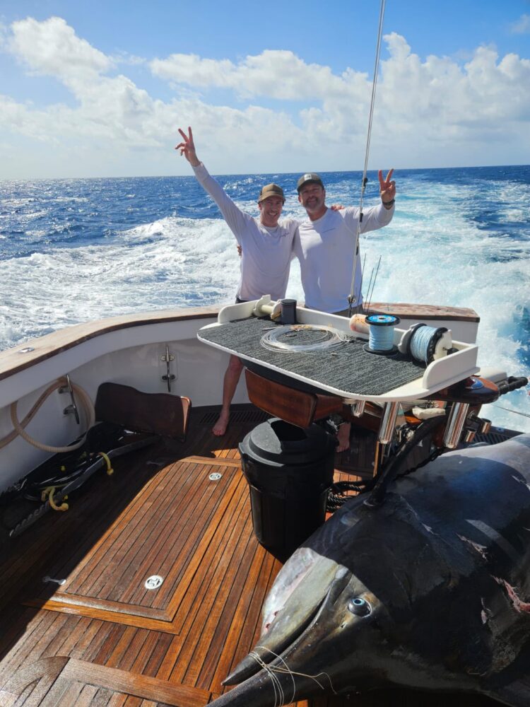 Two men on the deck of a boat making peace signs with a large marlin visible in the foreground during a corporate Christmas party in Sydney.