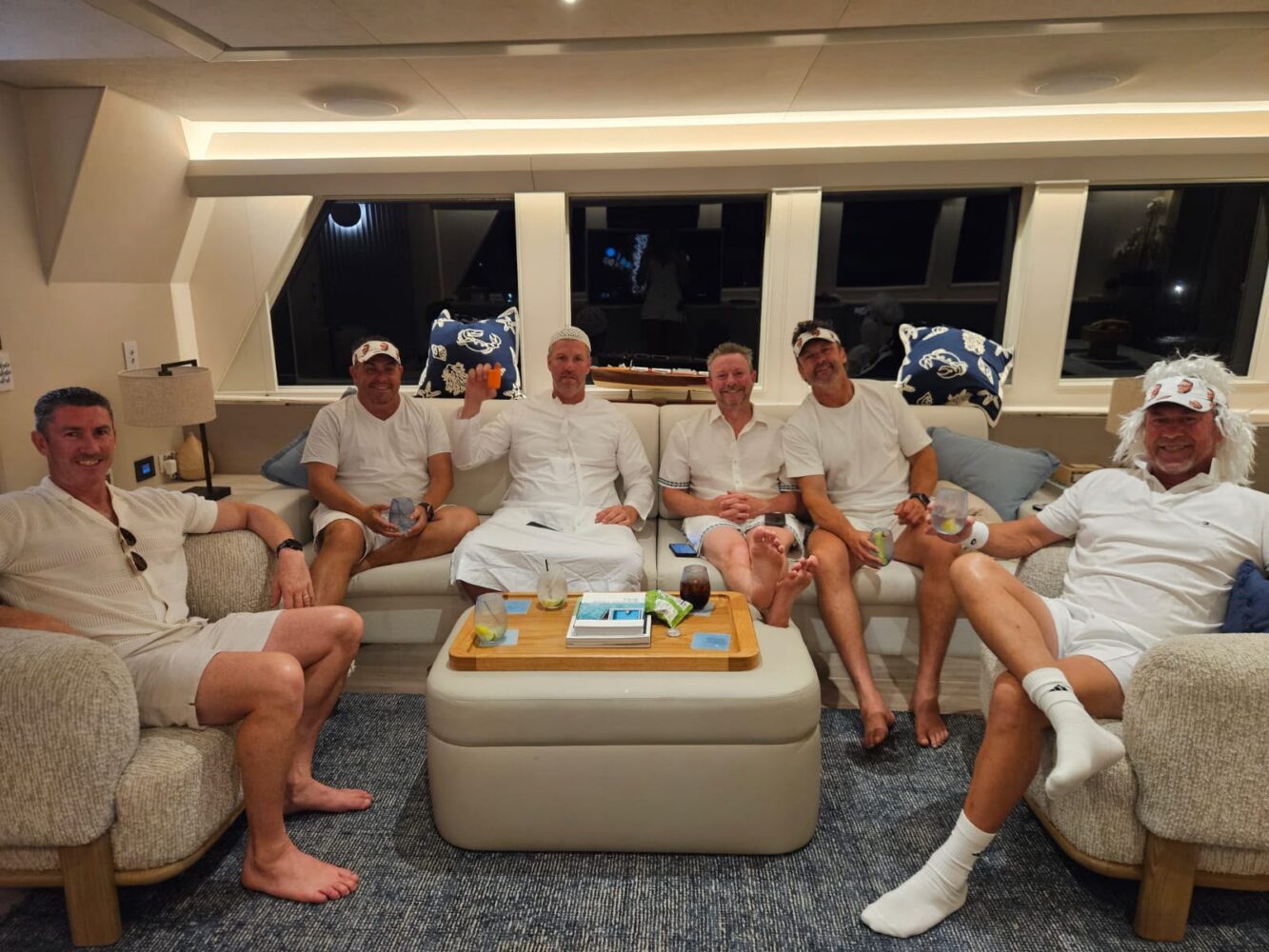 Five men in white casual attire relax with drinks in a yacht lounge during a corporate Christmas party in Sydney.