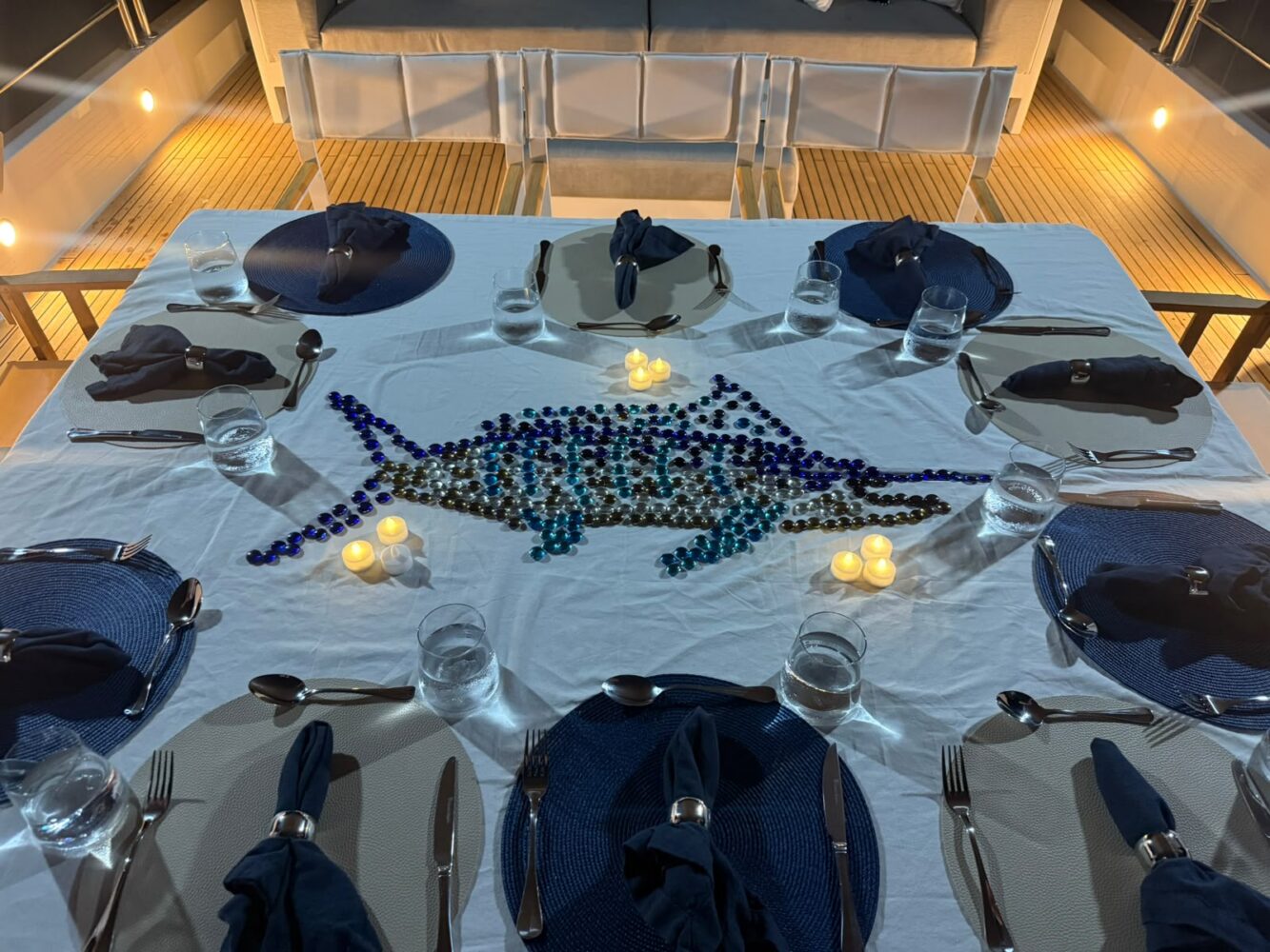 A table set for eight with a white tablecloth, dark blue placemats, and napkins in rings, featuring a centerpiece of blue glass beads shaped like a fish, perfect for a corporate Christmas party in Sydney.