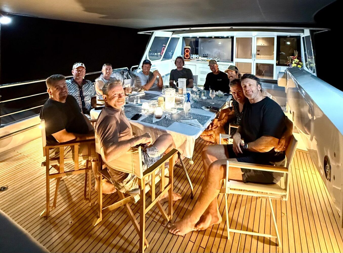 Ten men sitting around a table on the deck of a boat during a corporate Christmas party in Sydney at night.